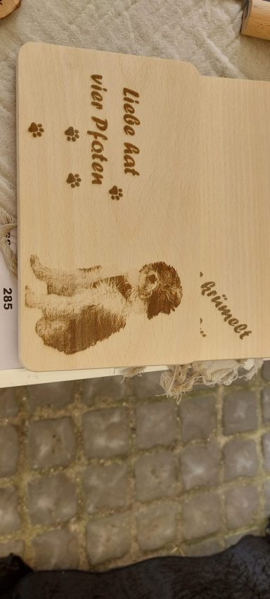 Helles Holzbrettchen mit graviertem Hundeporträt, Pfotenabdrücken, dem Spruch „Liebe hat vier Pfoten“