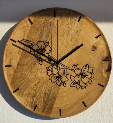 Runde Holzwanduhr mit goldbrauner Maserung, schwarzen Zeigern und drei großen, diagonal angeordneten gravierten Blüten.