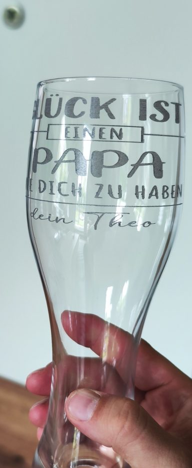 Klares Weizenglas in einer Hand, graviert mit dem Spruch „Glück ist, einen Papa wie dich zu haben“ und der Widmung „dein Theo“.